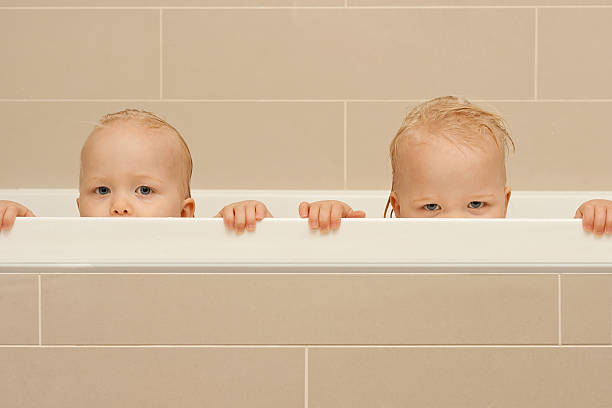 Identical twins toddlers peeking over the bath stock photo