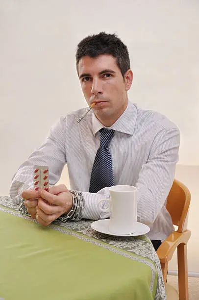 Professional businessman chained to prescription pills cigarette in his mouth coffee cup looking stressed and angry
