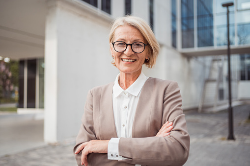 In the business portrait, we see a business woman standing upright, with her arms crossed. Her appearance suggests seriousness and confidence. Attire is professional and well put together, probably in accordance with the business dress code.