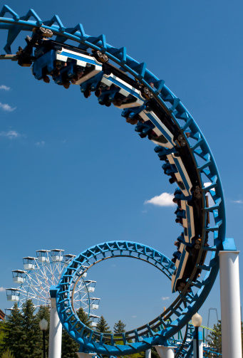 Cork-screw Rollercoaster and Ferris-Wheel at amusement park. Slight motion blur on Rollercoaster cars