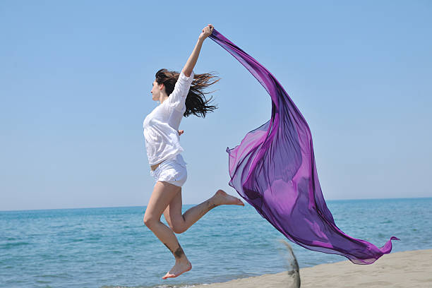 istock beautiful young woman on beach with scarf 155248046