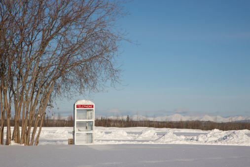 Lone phone booth stands in an open field covered with snow.