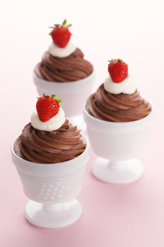 Three chocolate mousses with whipped cream and strawberries.