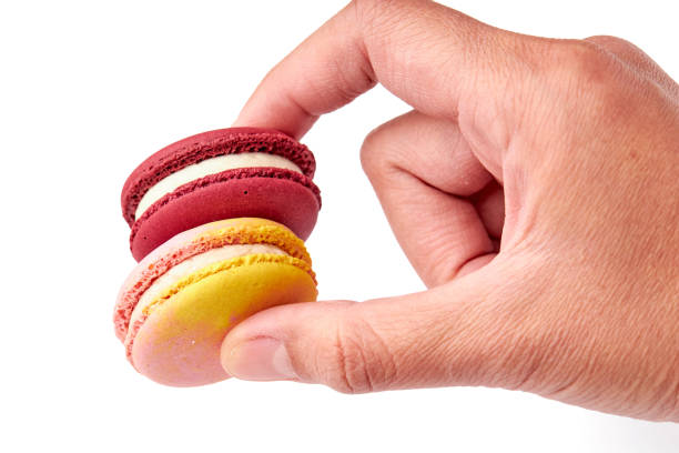 istock Hand holding red and pink macaron isolated on white background. Side view of macaron. 1552560184