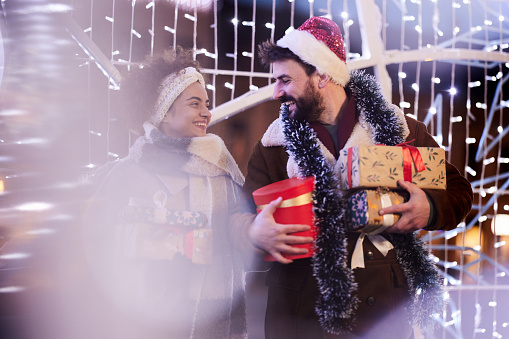 Carefree couple communicating while holding gifts during Christmas night in the city.