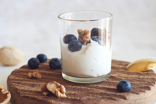 Yogurt with blueberries and walnuts in a glass on a board