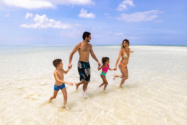 istock Happy family having fun while holding hands and running through sea in summer day. 1552577949