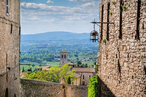 A beautiful and peaceful landscape of the countryside around the medieval town of Assisi, in Umbria, with cultivated fields, farms, olive groves, orchards and woods. In the centre, the bell tower of the Abbey Church of San Pietro, built in Romanesque-Gothic style between the 10th and 13th centuries. Over the centuries Assisi and the spirituality of its sacred places have become a symbol of peace, a point of reference for tolerance and solidarity between peoples and between the different confessions of the world. The Umbria region, considered the green lung of Italy for its wooded mountains, is characterized by a perfect integration between nature and the presence of man, in a context of environmental sustainability and healthy life. In addition to its immense artistic and historical heritage, Umbria is famous for its food and wine production and for the high quality of the olive oil produced in these lands. Since 2000 the Basilica and other Franciscan sites of Assisi have been declared a World Heritage Site by UNESCO. Image in high definition quality.