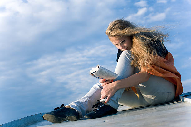 Young beautiful girl reading book outdoors stock photo