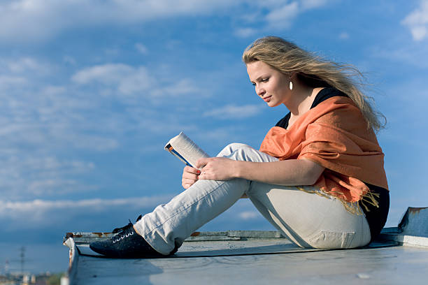 Young beautiful girl reading book outdoors stock photo