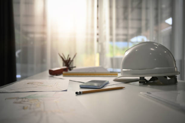 Safety helmets, blueprints and smartphone on the engineering desks. Engineering tools, workspace concept. stock photo