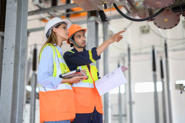 istock Caucasian electrical female engineer and male Asian technician worker with personal safety equipment using digital tablet check list operating or check status of high voltage circuit breaker switch of high voltage electric transformer sub station. 1552631946