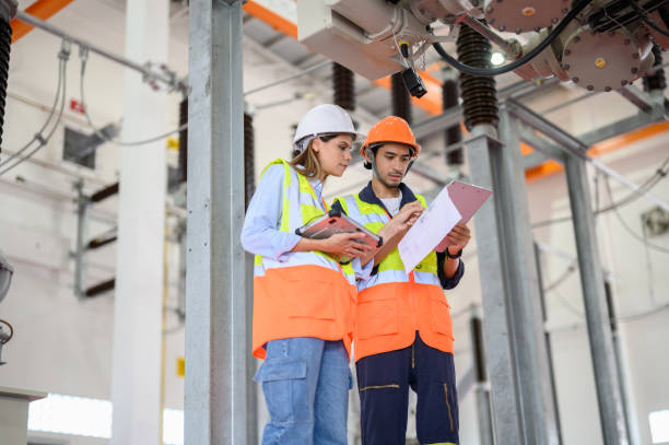 istock Caucasian electrical female engineer and male Asian technician worker with personal safety equipment using digital tablet check list operating or check status of high voltage circuit breaker switch of high voltage electric transformer sub station. 1552632459