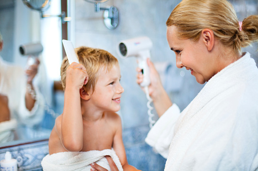 Mother drying up child's hair with a hair dryer in a bathroom after bath.