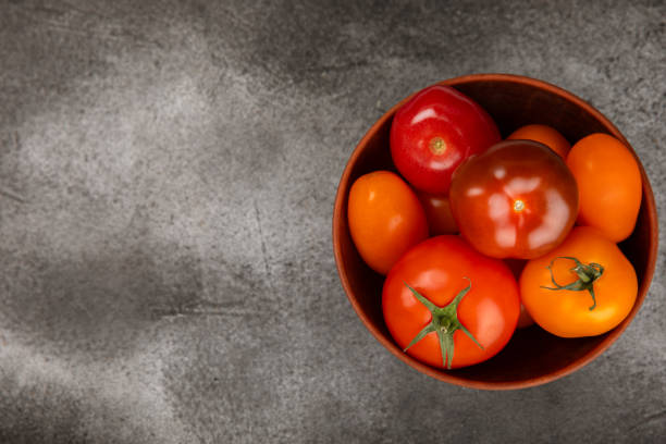 Tomatoes on marble texture background. Cherry tomatoes, yellow, pink, brown and black tomatoes in a bowl. Organic vegetables, harvesting.Vegan. Fresh ripe tomatoes. copy space.