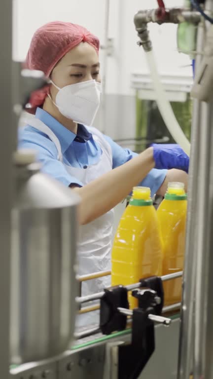 Asian Chinese female juice factory worker sealing bottle cap of orange juice in production line