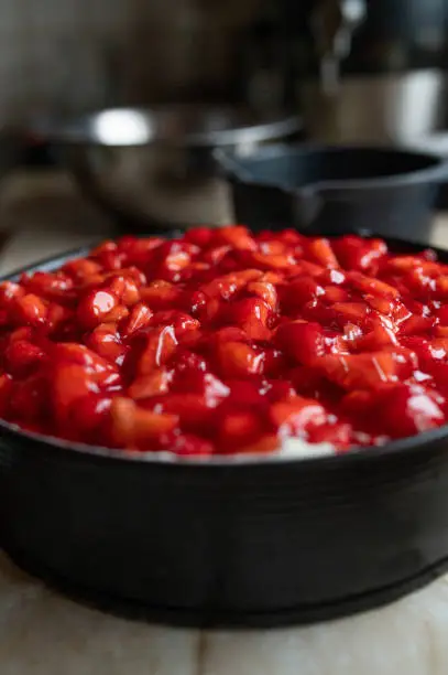 Fresh glazed strawberry cream cake in a round cake tin or pan on kitchen counter. Closeup, front view