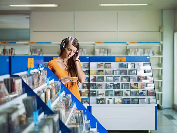 caucasian woman with headphones, choosing cd in music shop. Horizontal shape, front view, waist up, copy space