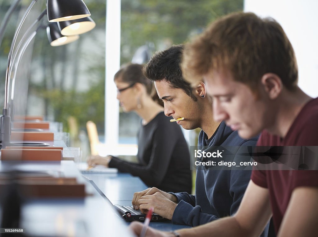 group of three people in library male college student sitting in library, typing on laptop computer. Horizontal shape, side view, waist up Group Of People Stock Photo