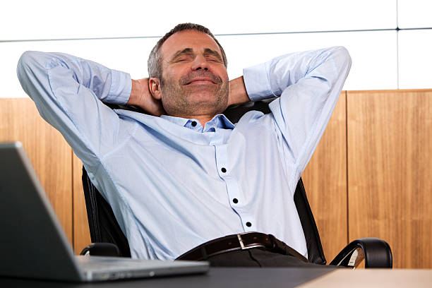 Smiling manager relaxing in office chair. Happy senior businessman leaning back in his office chair. bending over backwards stock pictures, royalty-free photos & images