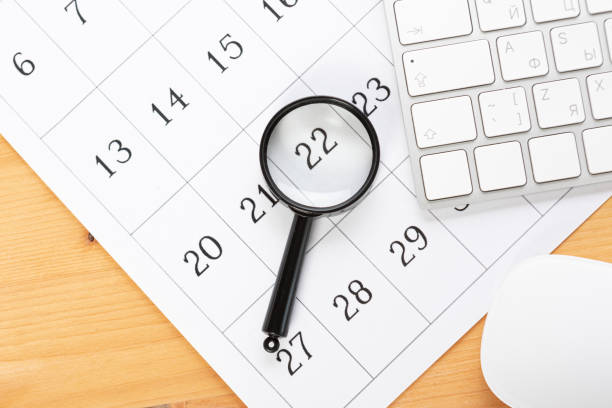 istock Calendar and reminders with magnifying glass, work from home online. desktop calendar with stationery and pen pencil, keyboard. mark a holiday trip or plans in a diary at the office desk. 2023 calendar reminder concept. 1552697227