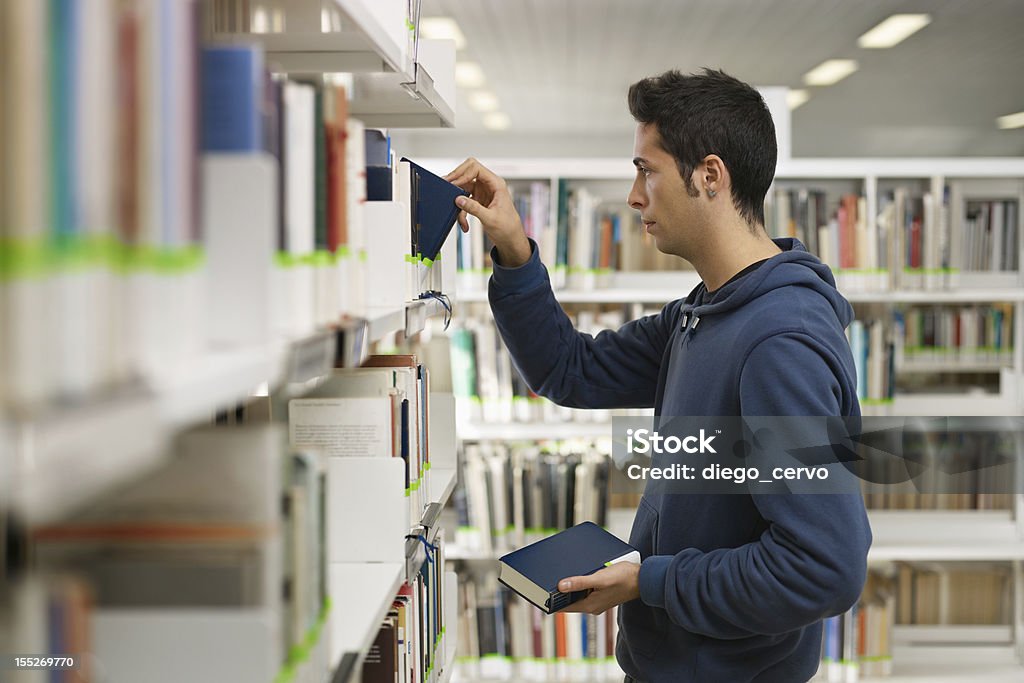 Uomo scegliendo il libro in biblioteca - Foto stock royalty-free di 20-24 anni