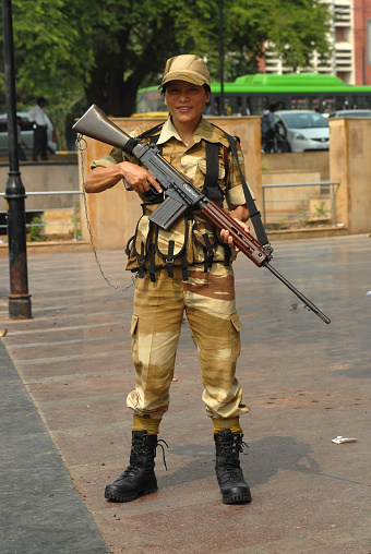 Indian female soldier in camouflage uniform holding a big rifle on a sunny day in the old part of New Delhi, India