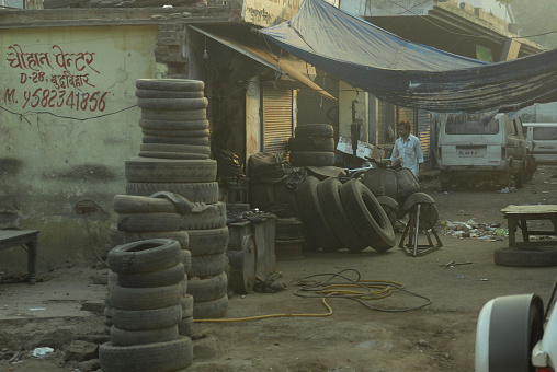 Stacked piles of old used tires outside a tire repair shop on a sunny afternoon in New Delhi, India