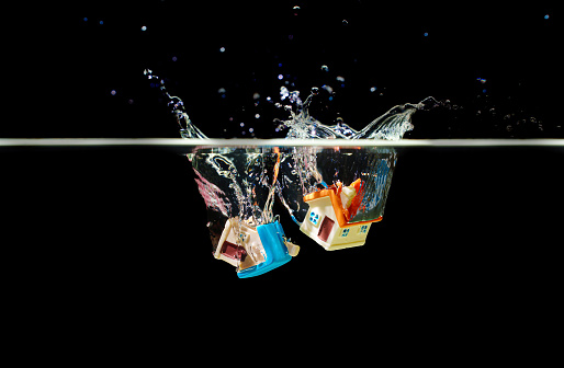 Close-up of two toy houses dropped underwater with splashes against black background. Coverage for accidental damage.
