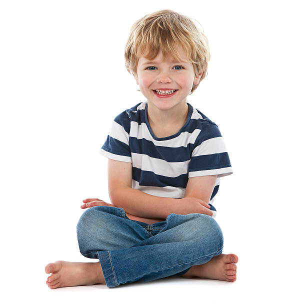 Small boy sitting crossed legged smiling on white stock photo