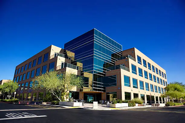 Stunning Scottsdale Arizona business building on blue backgrounded sky with matching blue glass windows beautifully landscaped with desert tolerant plant and trees on a clear day with set on a bright blue clear sky background.