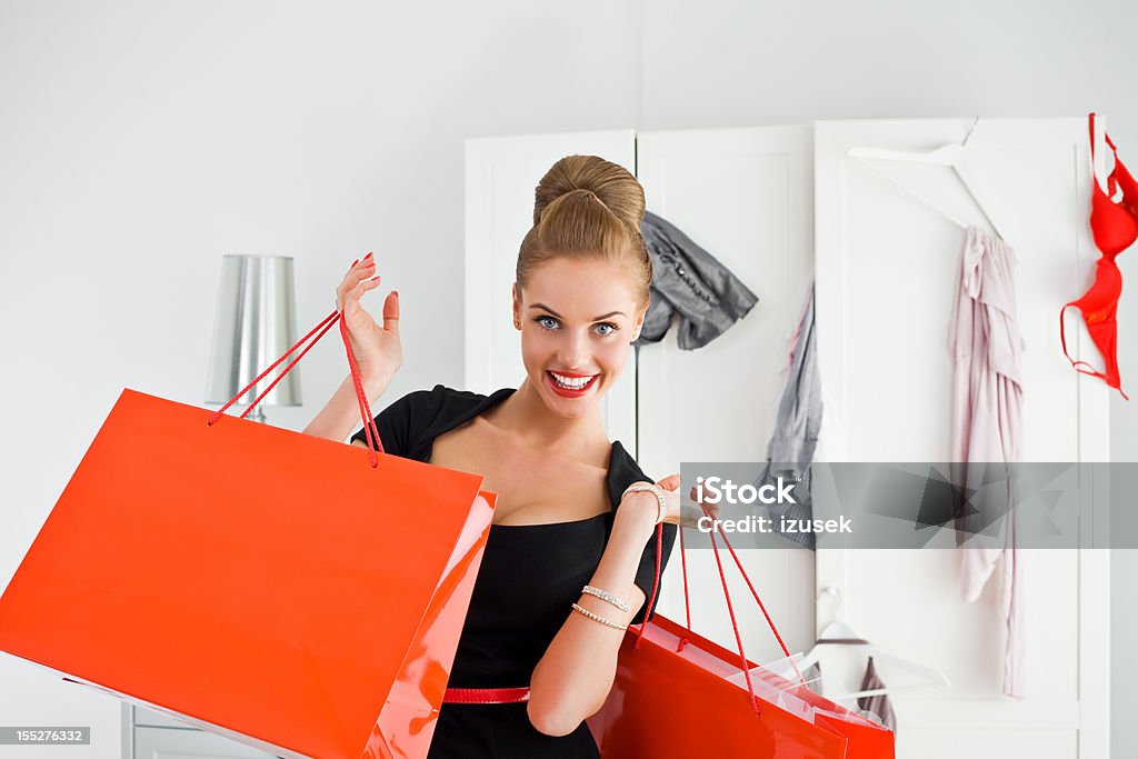Beautiful shopaholic Portrait of excited young adult woman holding red shopping bags in both hands with messy wardrobe in the background. smiling at the camera. 20-24 Years Stock Photo
