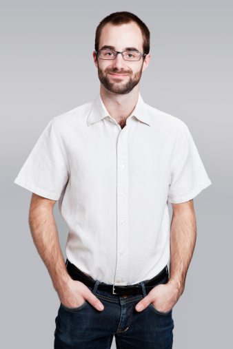 Contemporary bearded Caucasian worker in summer clothes wearing glasses with hands in pockets.