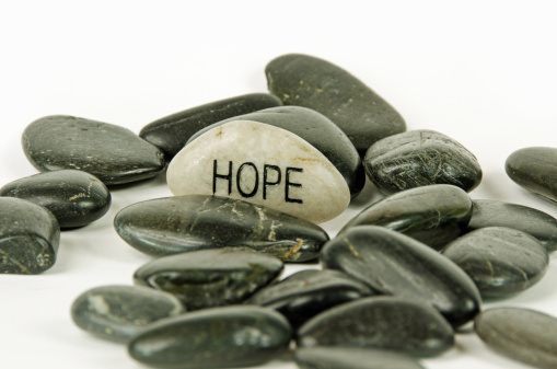 Dark colored rocks and a light rock with the word HOPE engraved into it. On a white background.