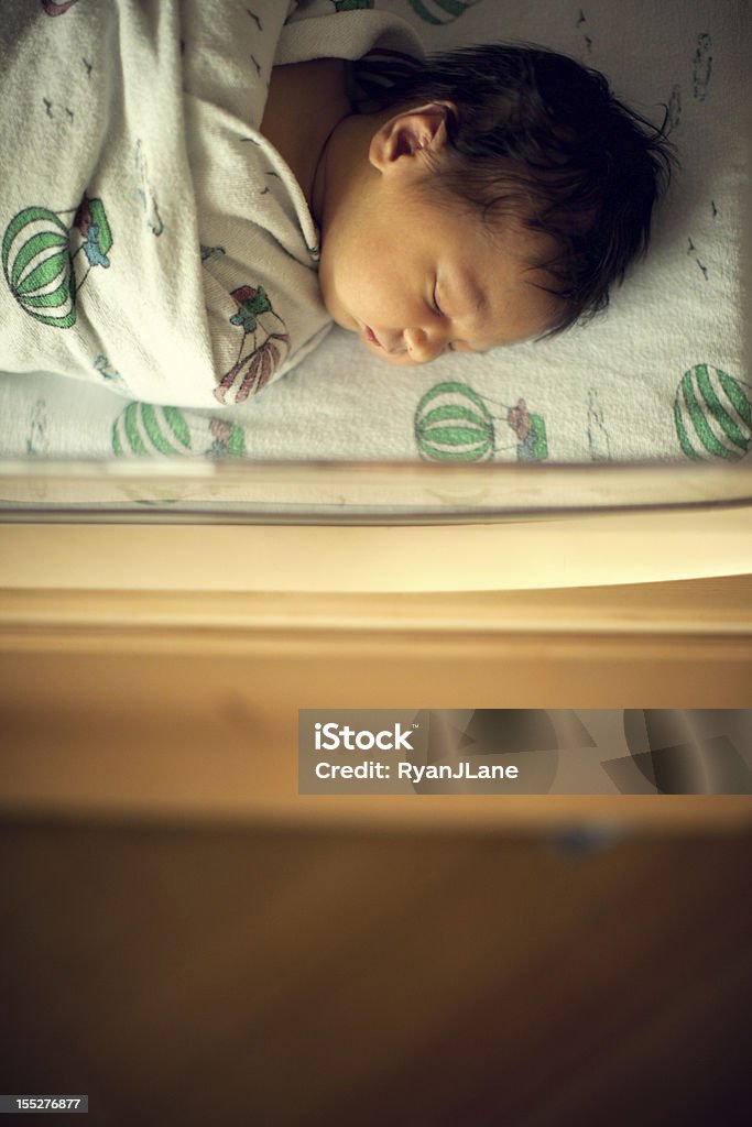 Newborn Sleeping Baby Boy in Hospital Bassinet A peaceful looking baby boy sleeps snugly in a clear plastic hospital bassinet, resting atop a wooden cart.  View from directly overhead in hospital room; vertical with copy space. Baby - Human Age Stock Photo