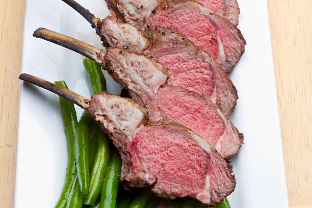 Rack of Lamb with Carrots and Green Beans Sliced Rack of Lamb cooked medium rare with baby Carrots and Green Beans on a white rectangular plate.  Lamb chops have been Frenched revealing the bare rib bone. rack of lamb stock pictures, royalty-free photos & images