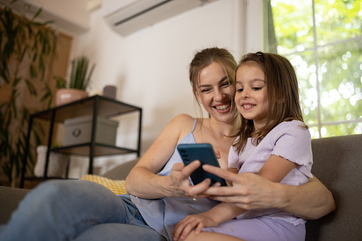 A young Caucasian mother and her daughter using a smartphone together in the living room at home