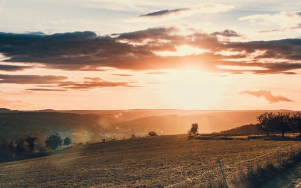 istock Beautiful summer evening with the sun setting behind a hillside and fields in the foreground. 1552795527