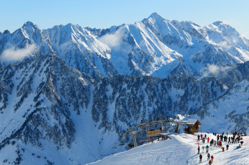 Winter Pyrenees is photographed at the Cauterets ski resort. Many skiers have been transported with Grand Barbat Chair lift up the snowy slope at the Cirque du Lys. There is range of mountains (Soum de Mauloc) in the background.