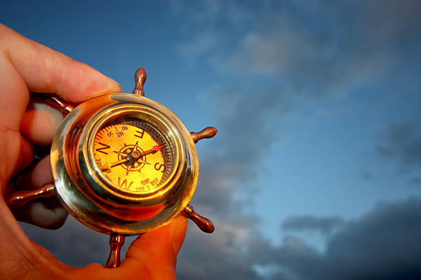 One hand holding a compass and a cloudy sky Hand holding compass. rudder stock pictures, royalty-free photos & images