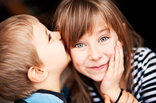 Little boy whispering to her sister's ear.
