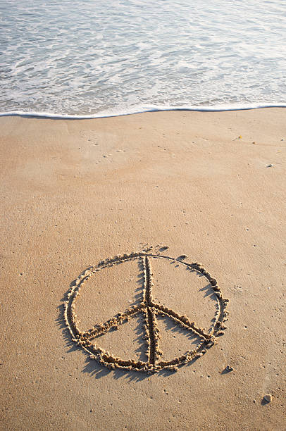 Peace symbol drawn in beach sand near ocean's edge stock photo