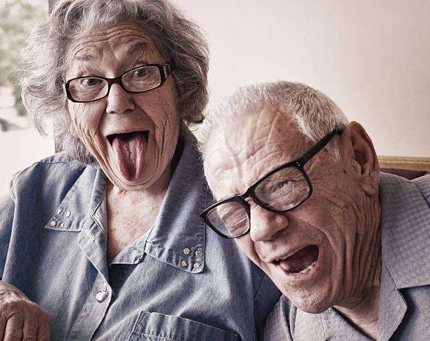 Grandma and Grandpa Making Funny Tongue Wagging Faces A crazy, fun-loving elderly octogenarian senior adult married husband and wife couple sitting together in a restaurant are making silly funny tongue wagging faces. Both Grandma and Grandpa are playful and laughing - they love mugging for the camera. Desaturated. grandma portrait stock pictures, royalty-free photos & images