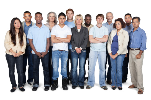 A multi-ethnic group of business professionals are standing together in a large group at the office. They are smiling and looking at the camera.