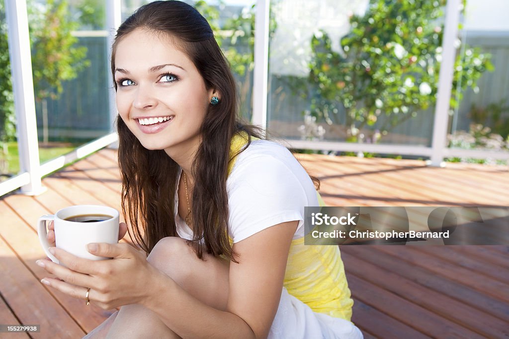 Sonriente Joven mujer sosteniendo una taza de café - Foto de stock de Patio de madera libre de derechos