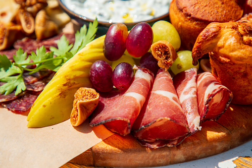 Close-up on prosciutto slices with assortment of delicatessen served on wooden board with corn bread, sliced fruit and olives, fine dining appetizer