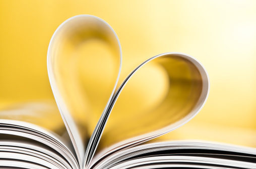 Book pages folded into a heart shape on yellow background. Copy space, horizontal, studio shot.