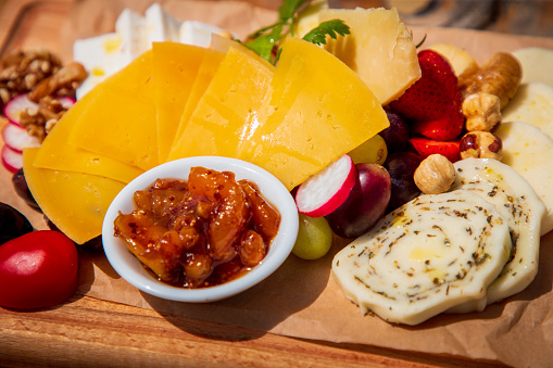 Assortment of delicious cheese served on wax paper on wooden board with fresh fruit, olives and nuts, sweet candied fruit cream in a bowl, fine dining appetizer