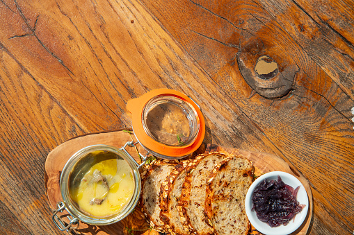 Above goose liver pate in a jar with slices of wholegrain bread, served on wooden board with fruit jam on the table in fine dining