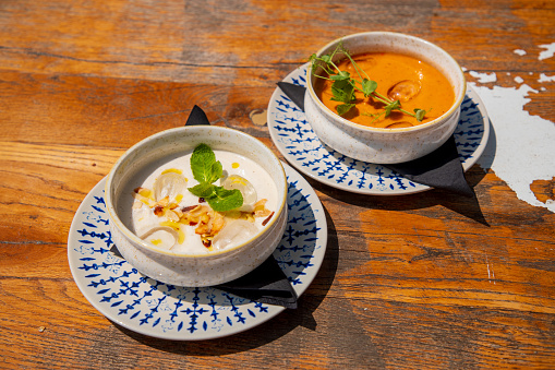 White cream soup and pumpkin potage served in bowls on wooden table in fine dining